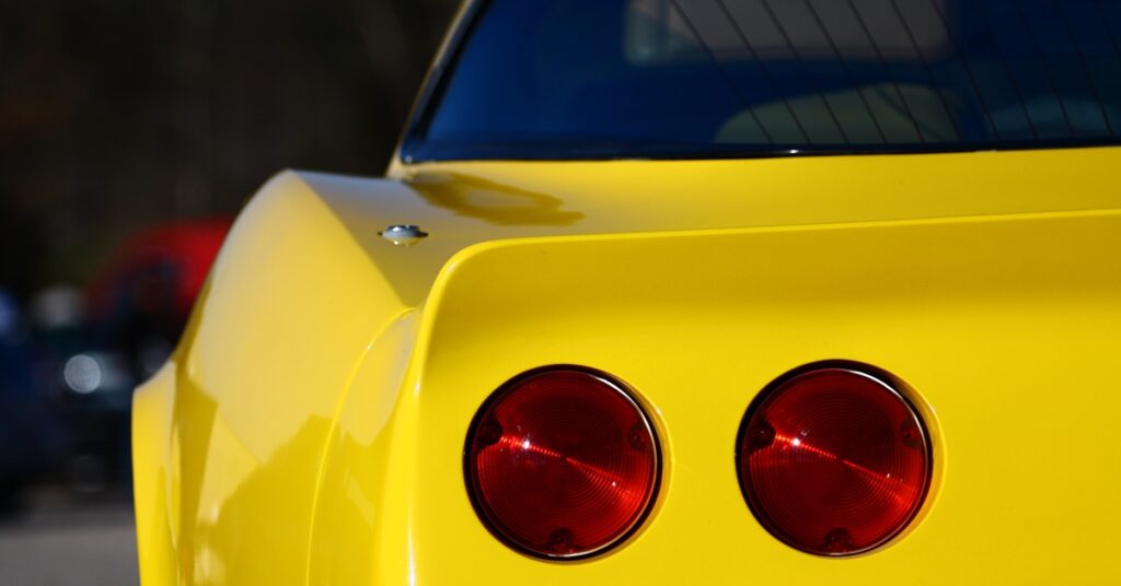 An extreme close-up of the backside of a yellow Corvette and its two small, red back lights that are off.
