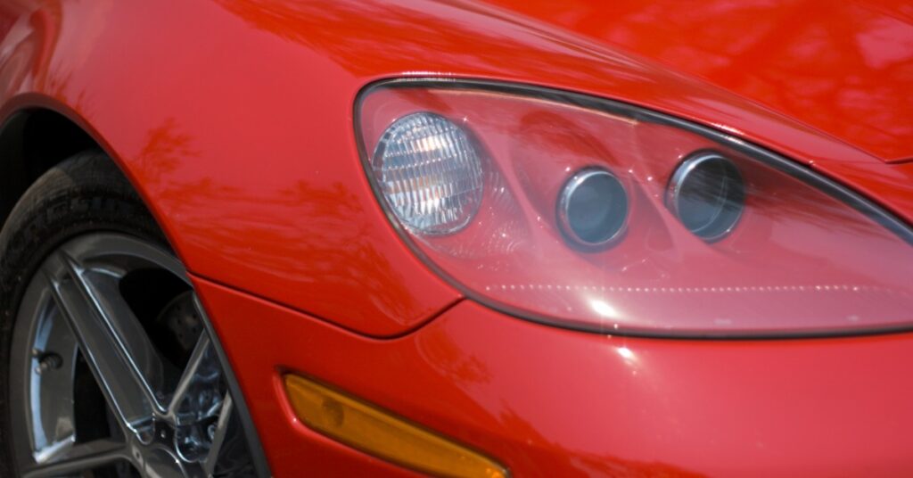 Close-up of red Corvette sports car headlight and front fender with chrome wheel and amber side marker.