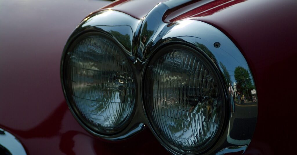 Detailed view of classic red car front featuring dual circular headlights and polished chrome housing