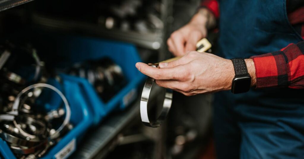 Close-up of a technician in blue overalls measures a metal ring with a caliper beside industrial machine parts.