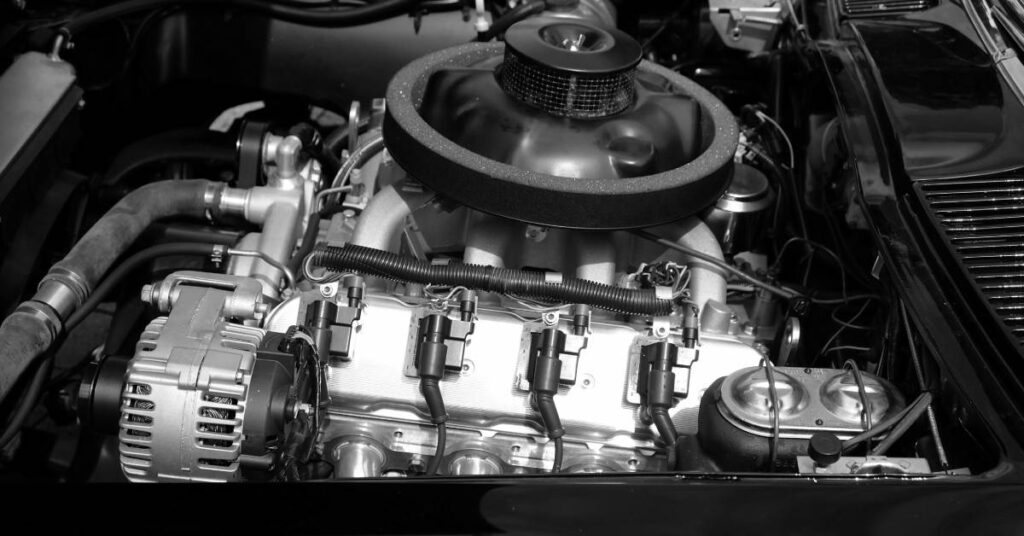 Close-up of car engine bay in monochrome, showing round air intake, spark plug wires, belts, and alternator.