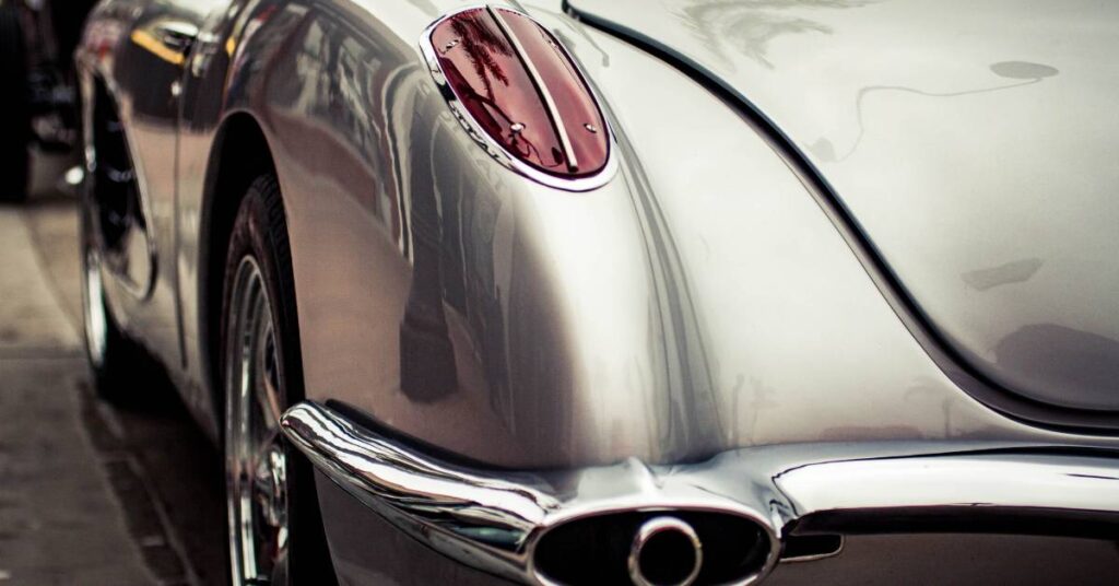Vintage silver car detail with rounded rear panel, chrome trim, and oval exhaust under glossy bodywork.