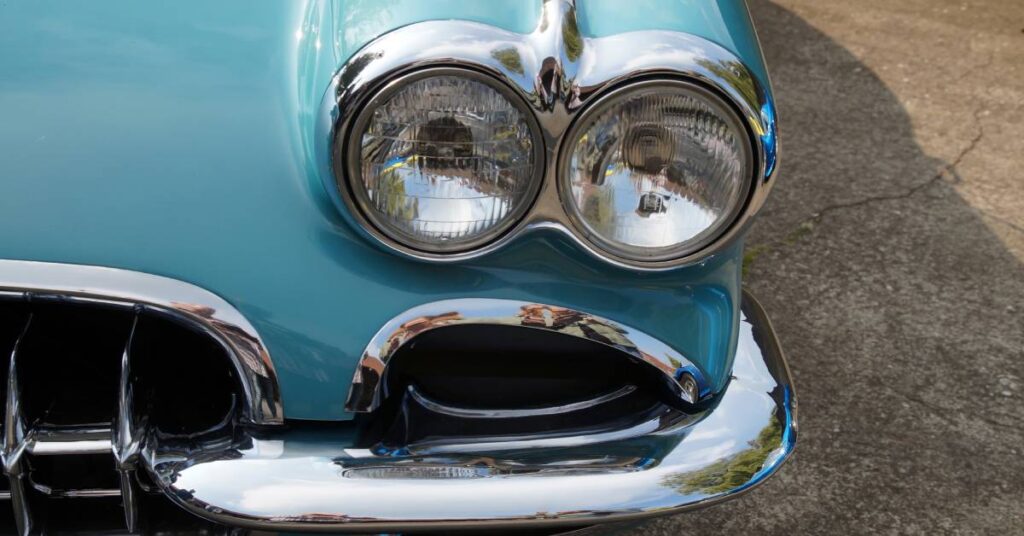 Classic turquoise Corvette nose with twin headlights and polished chrome trim parked on a paved street.