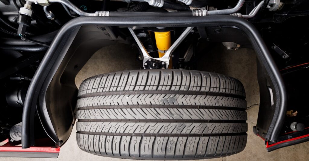 Close-up of car tire and suspension system, showing tread detail, shock absorber, and metal frame components.