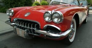 Close view of red vintage convertible with chrome grille and round headlights parked on tree-lined city street.