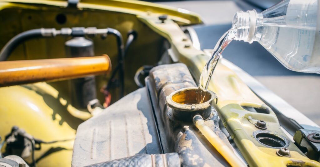 Water flows from a plastic bottle into an open car radiator, with engine hoses and yellow bodywork visible.