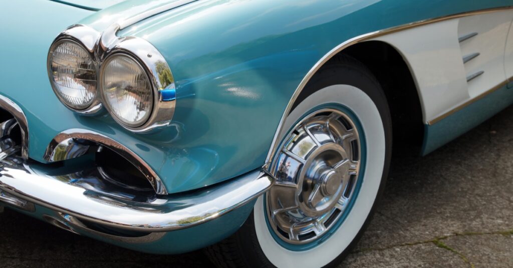 Turquoise vintage car shown from the front side, featuring twin headlights, a chrome bumper, and a whitewall tire.