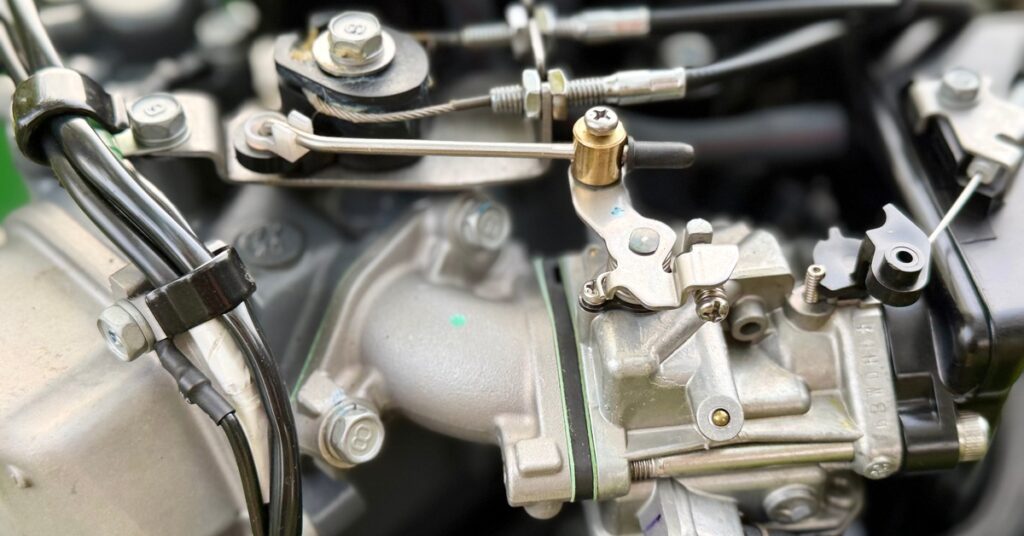 Detailed view of metal engine hardware showing a throttle linkage, cables, fasteners, hoses, and fittings.