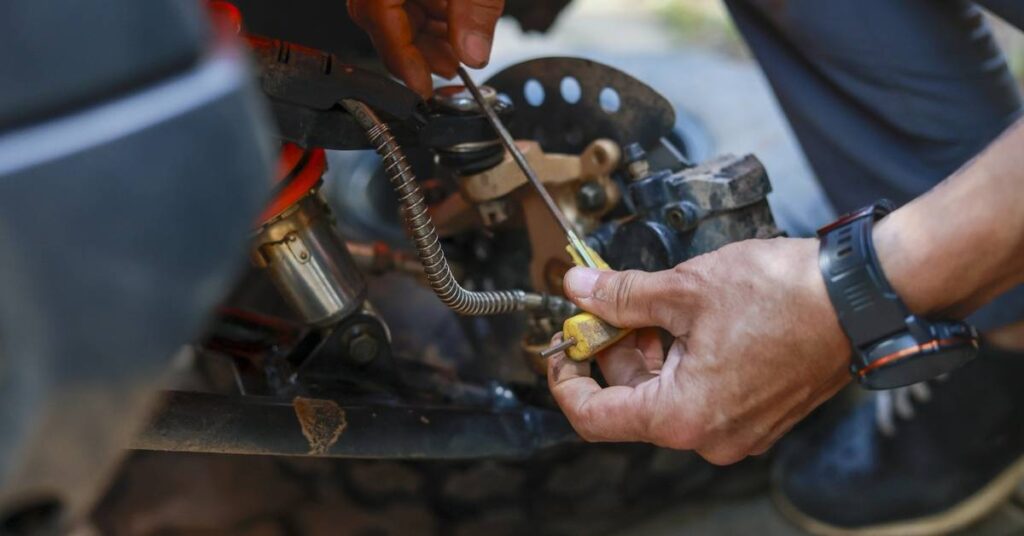 Close-up of hands repairing machinery with a screwdriver near exposed cables, springs, and metal components.