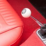 A detailed shot of the red interior of a vintage Corvette, focusing on the white and red manual gear shift.
