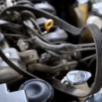 A close-up of a cracked and ripped car serpentine belt that's in the works of being repaired by a professional.