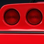 An extreme close-up of a 1980s Corvette sports car tail lights in the color cherry red. The car is off.