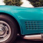 Close-up of vintage car side panel with teal paint, showing front wheel, chrome hubcap, and vent detail.
