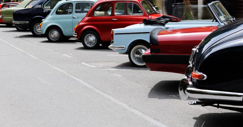A row of colorful vintage cars parked along a street, including compact red and blue classic models.