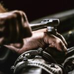 Mechanic adjusts bolt with ratchet tool on engine, focusing on detailed automotive repair under low light conditions.