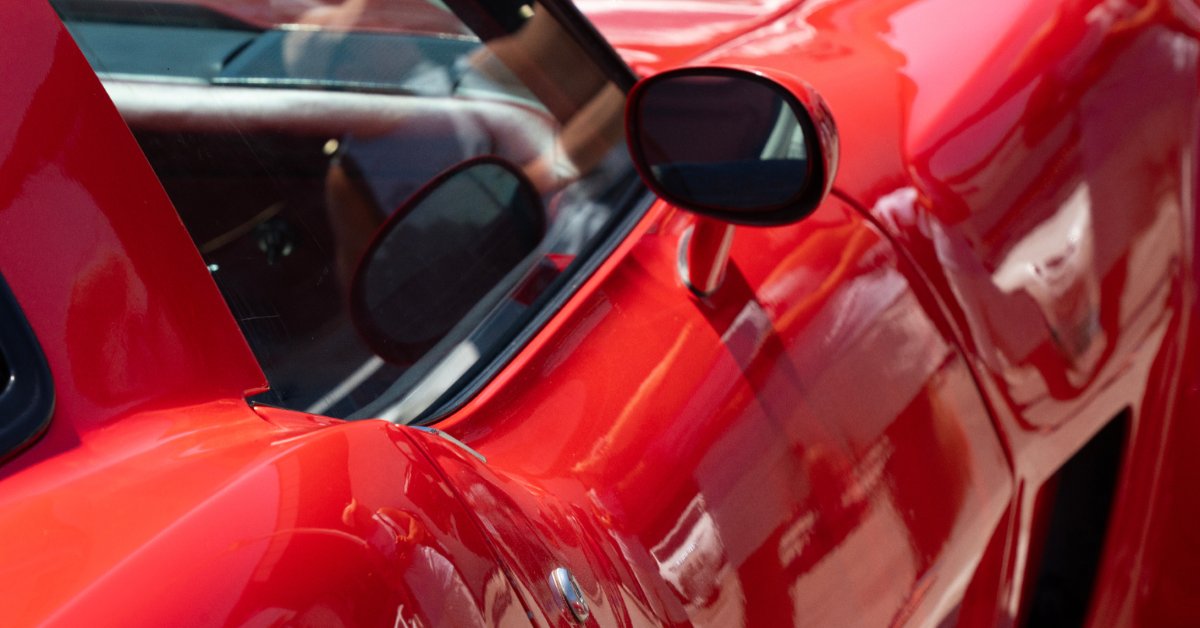 Detailed view of a red sports car exterior showing the side window, mirror, door handle, and shiny paint.
