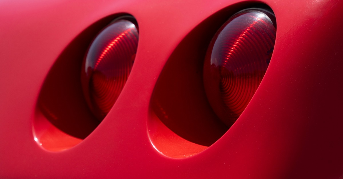 Close-up of two round red tail lights set into a glossy red car body, with curved recessed visible openings.