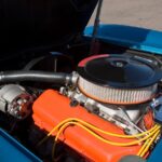 Detailed view of a blue car's engine bay, featuring orange covers, yellow ignition wires, and a black air cleaner.