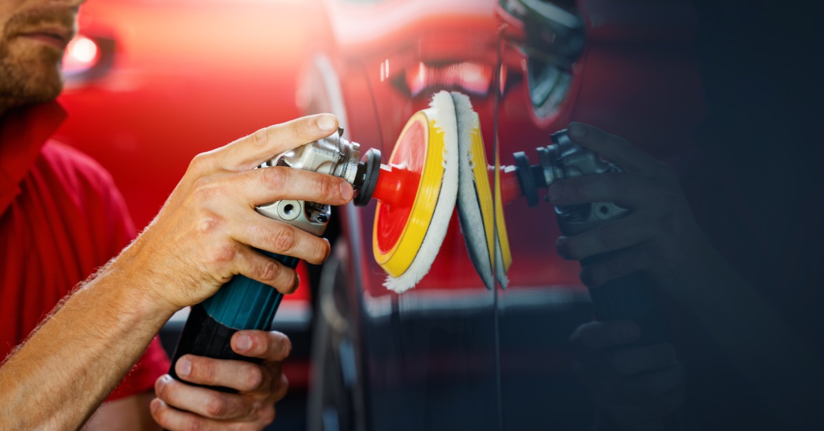 Close-up of hands operating a power polisher with a foam buffing pad on a black car door panel