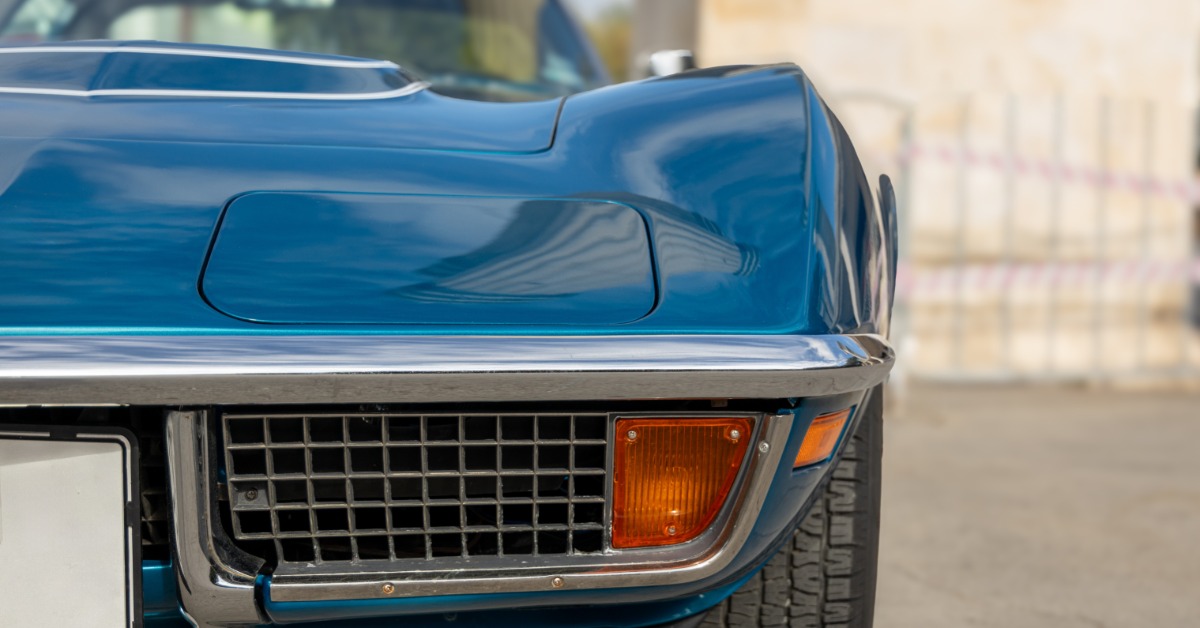 Front corner of a blue classic Corvette features a chrome-trimmed grille, amber signal light, and wide front tire.