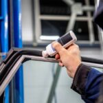 Close-up of a technician applying adhesive to the rubber trim around a vehicle window inside an auto repair shop.