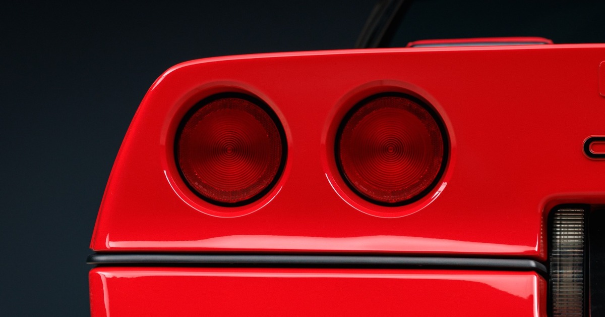 Close-up of the rear of a bright red sports car, featuring two circular taillights and a glossy finish against black.