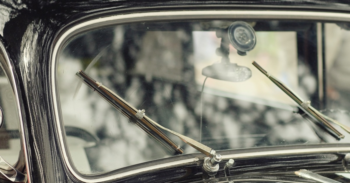 Front windshield of a classic black automobile featuring two angled metal wipers, chrome edging, and a split pane.